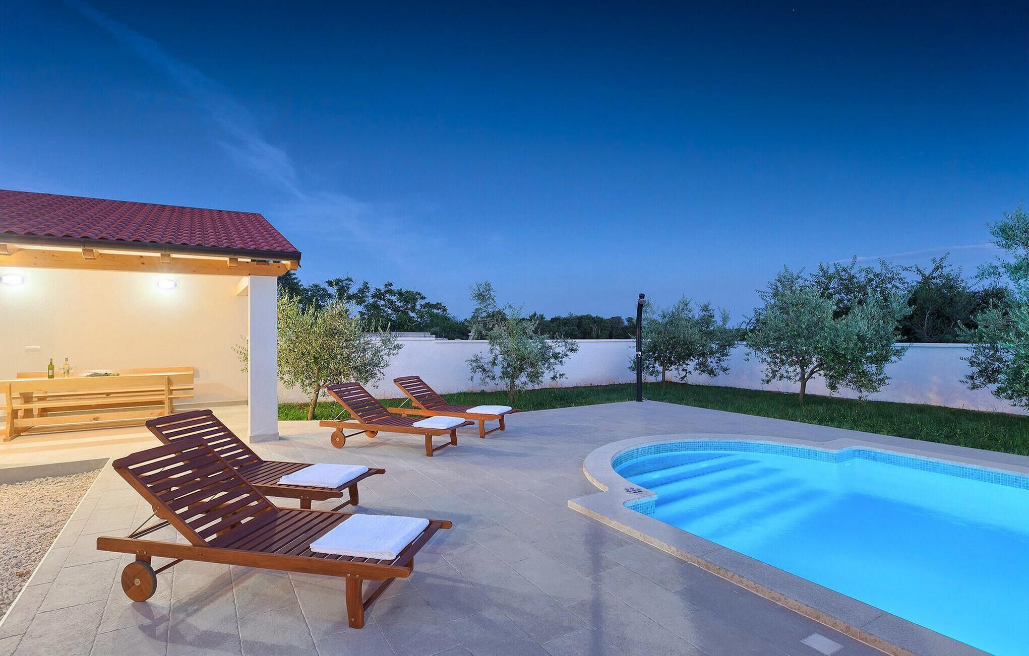 Área de piscina externa com espreguiçadeiras e um espaço coberto para sentar.