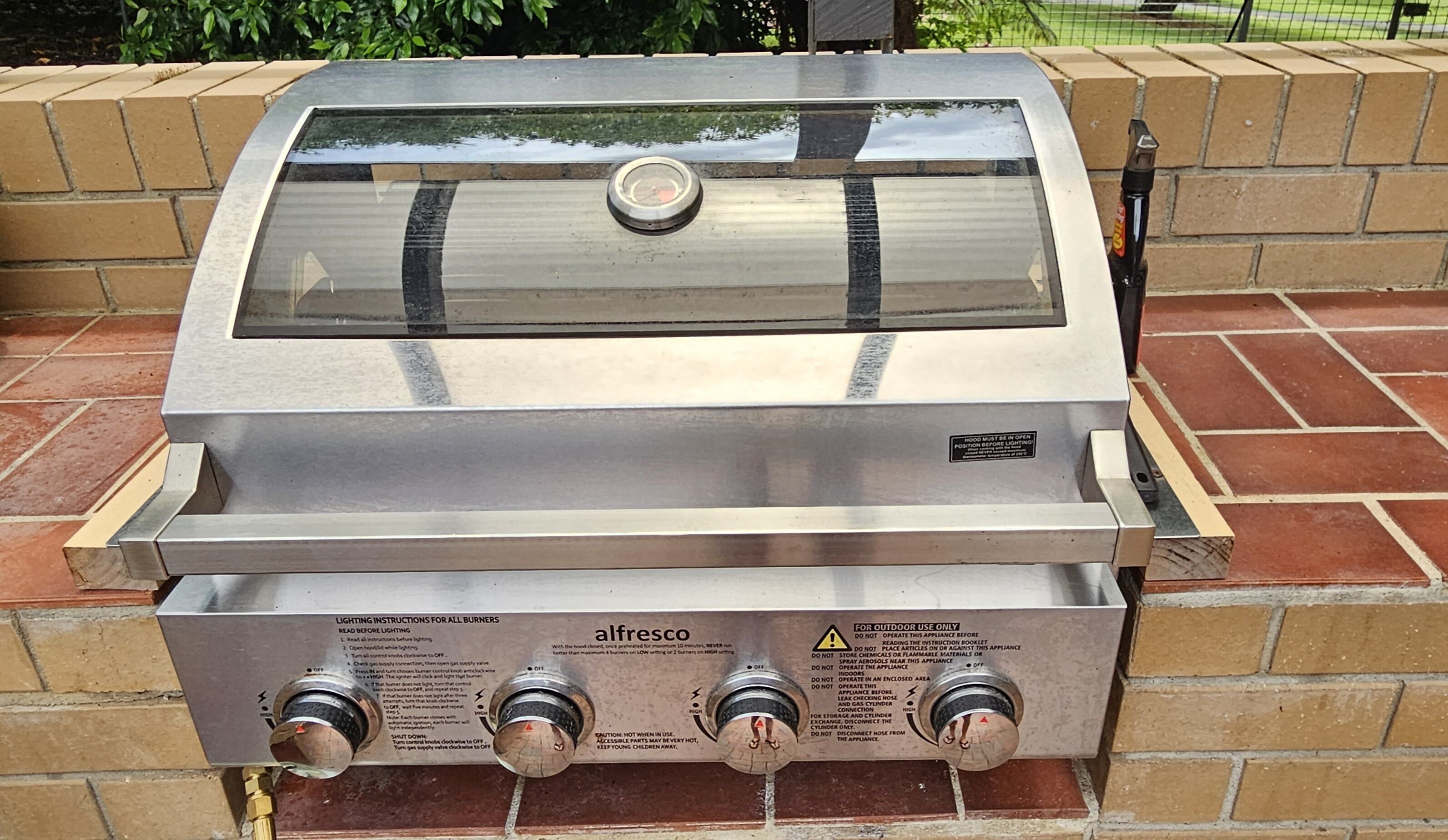 Un barbecue d’extérieur en acier inoxydable, doté d’un couvercle en verre, de boutons de contrôle et d’une étiquette d’avertissement.