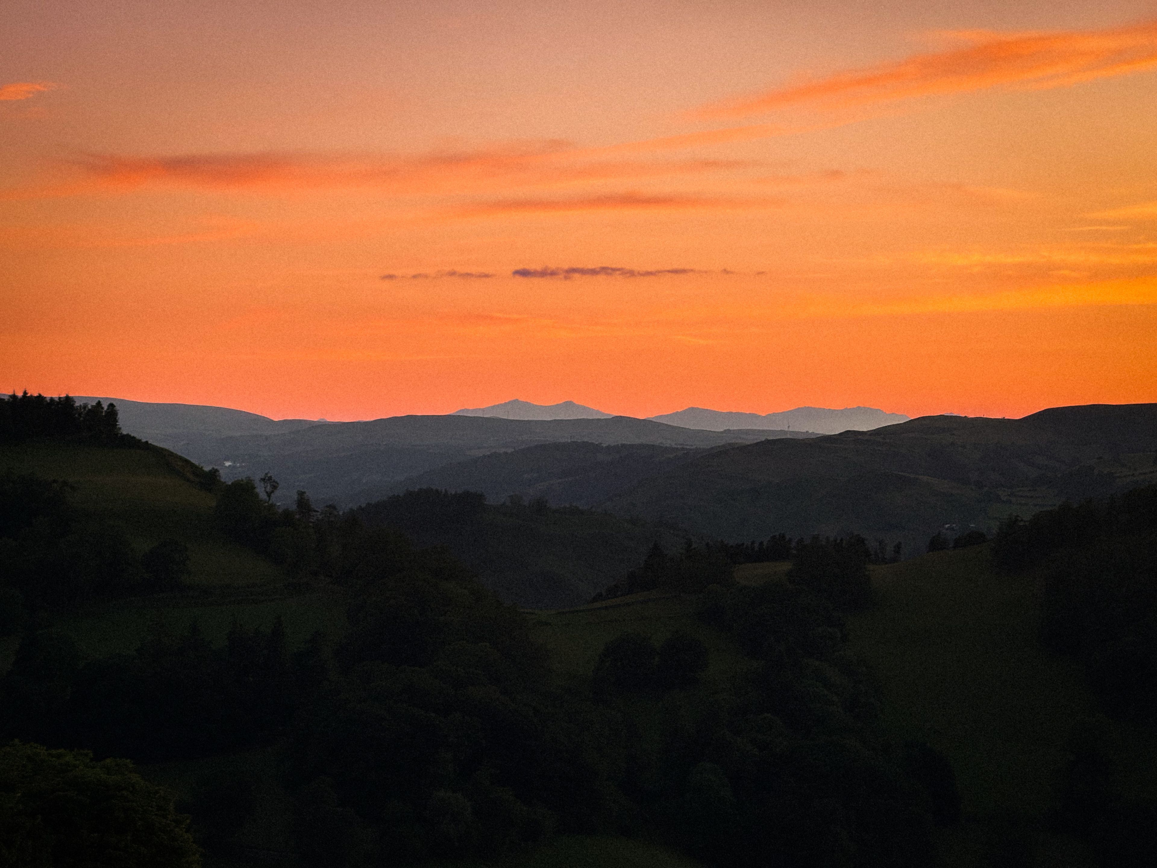 Et landskab med bløde bakker og en solnedgang.
