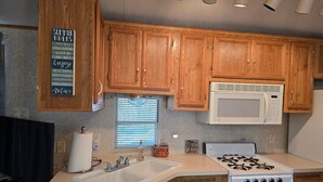 A kitchen with wooden cabinets, a white microwave, a stove, and a sink.