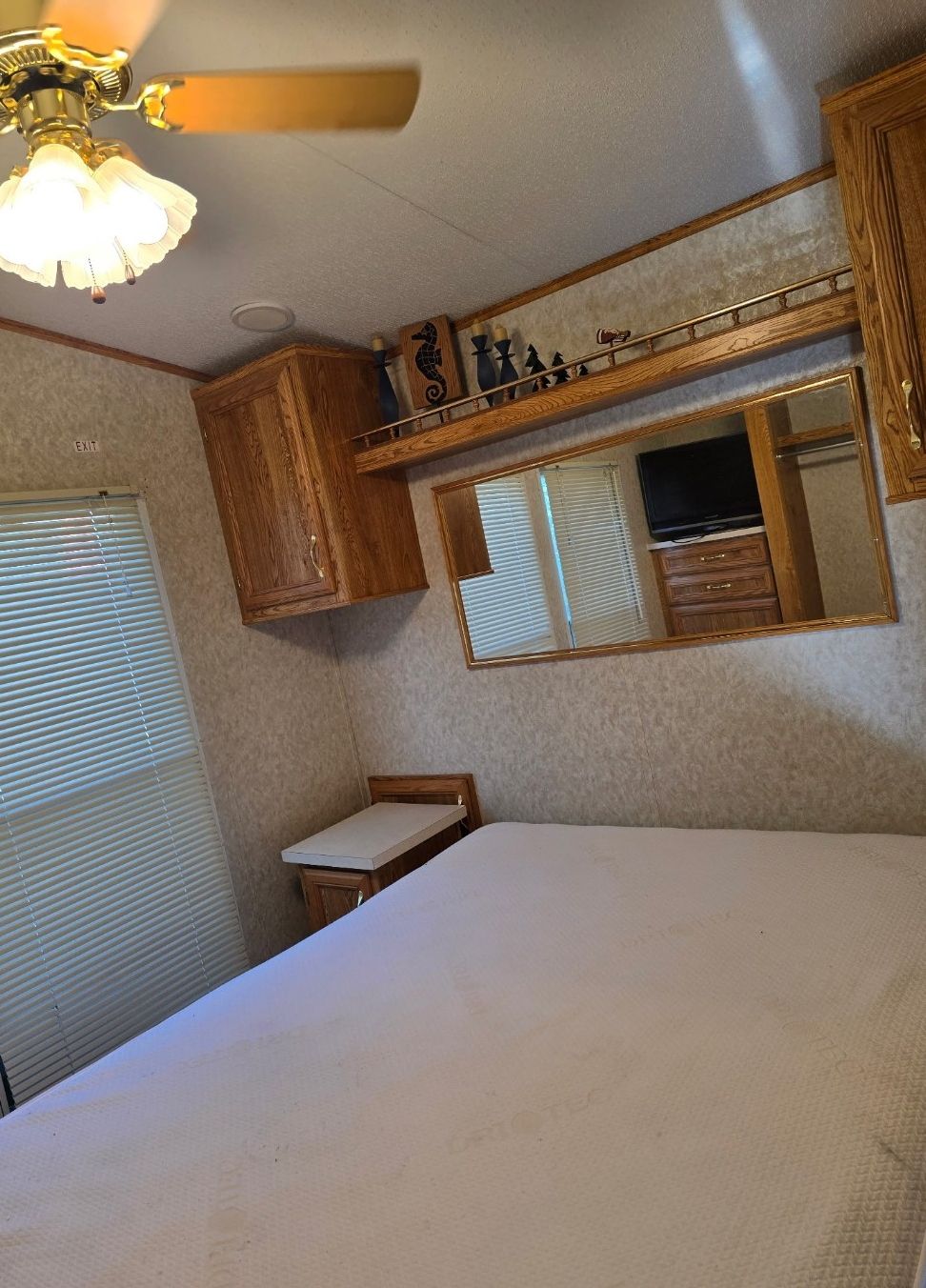 Une chambre à coucher avec un lit, un ventilateur de plafond, un miroir et des armoires en bois.