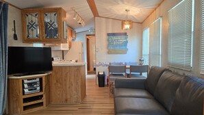A cozy RV interior with a wooden kitchenette, a flat-screen TV, a dining area with a table and chairs, and a large couch.
