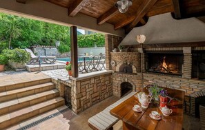 An outdoor patio with a stone fireplace, a wooden table with tea set, and a pool in the background. - Lovely home in Krsan with WiFi (Krsan)