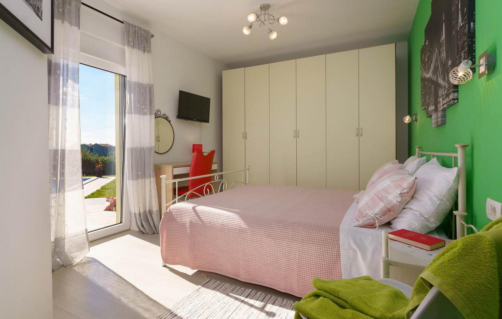 Ein Schlafzimmer mit einem Bett, einem Kleiderschrank, einem Fernseher und einer grünen Wand.