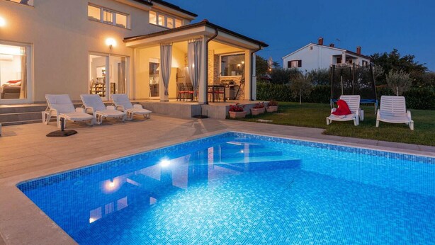 Una casa moderna con piscina, mobiliario de exterior y un patio bien iluminado.