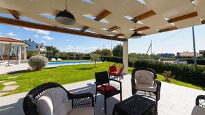 Un espacio de estar al aire libre techado con mobiliario de mimbre y una lámpara colgante.