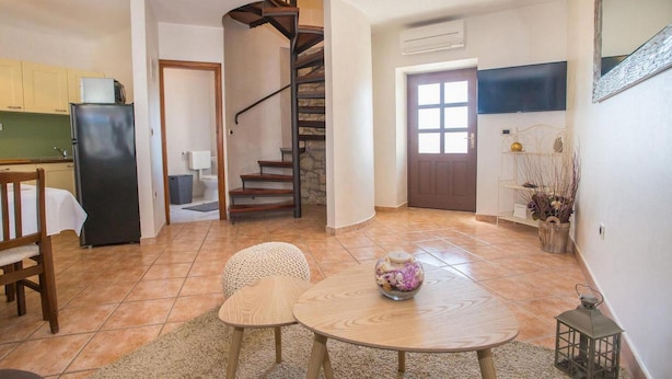 Uma sala de estar ampla com cozinha, uma mesa de jantar com duas cadeiras, uma escada e uma porta que dá para outro cômodo.