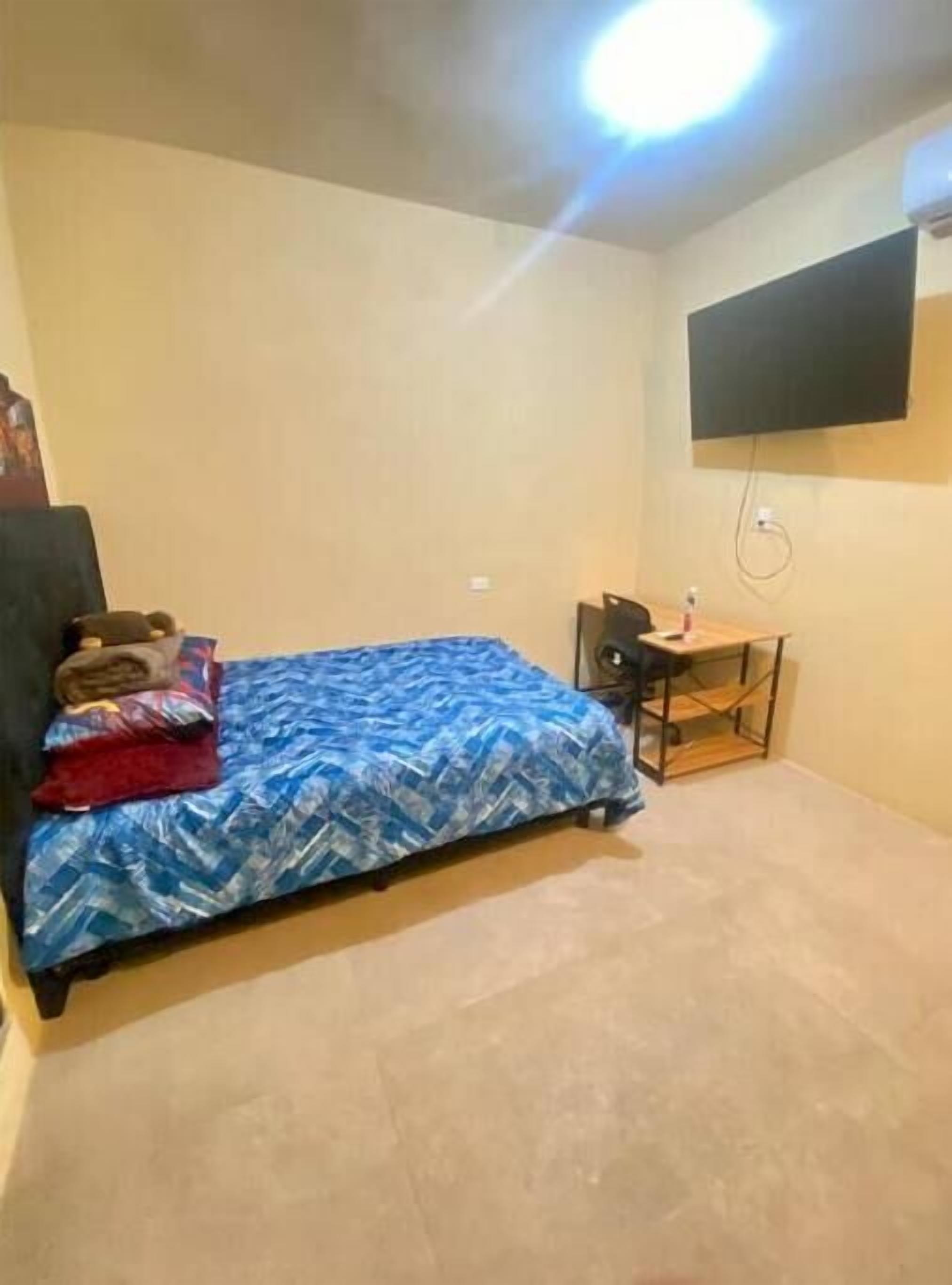 Un dormitorio con una cama, un escritorio y una televisión instalada en la pared.