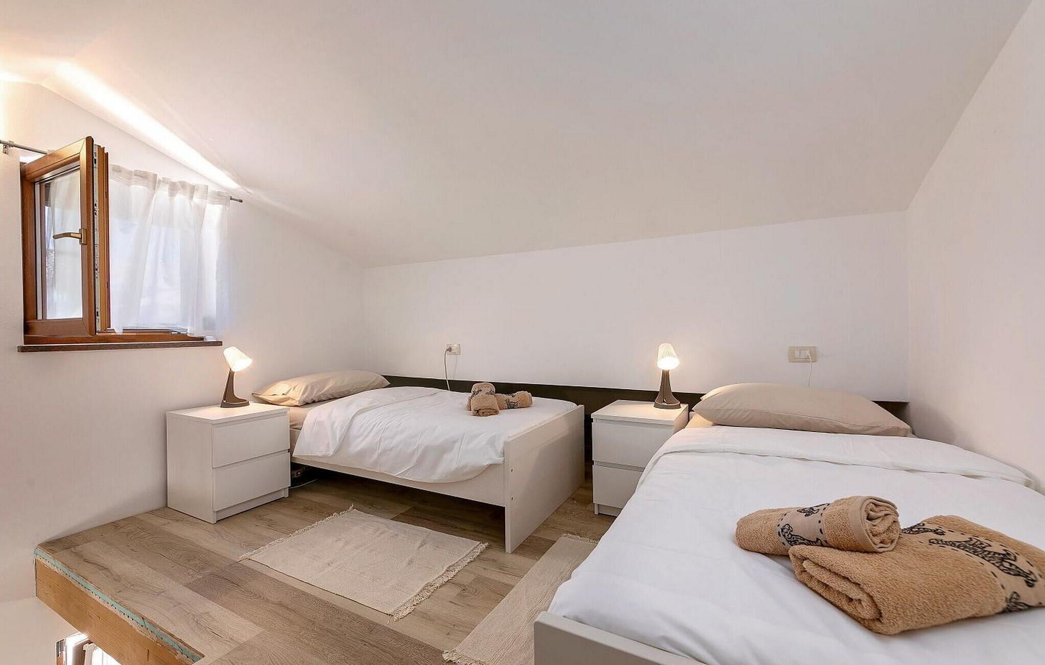 A bedroom with two single beds, bedside tables, a window with curtains, and a wooden floor.