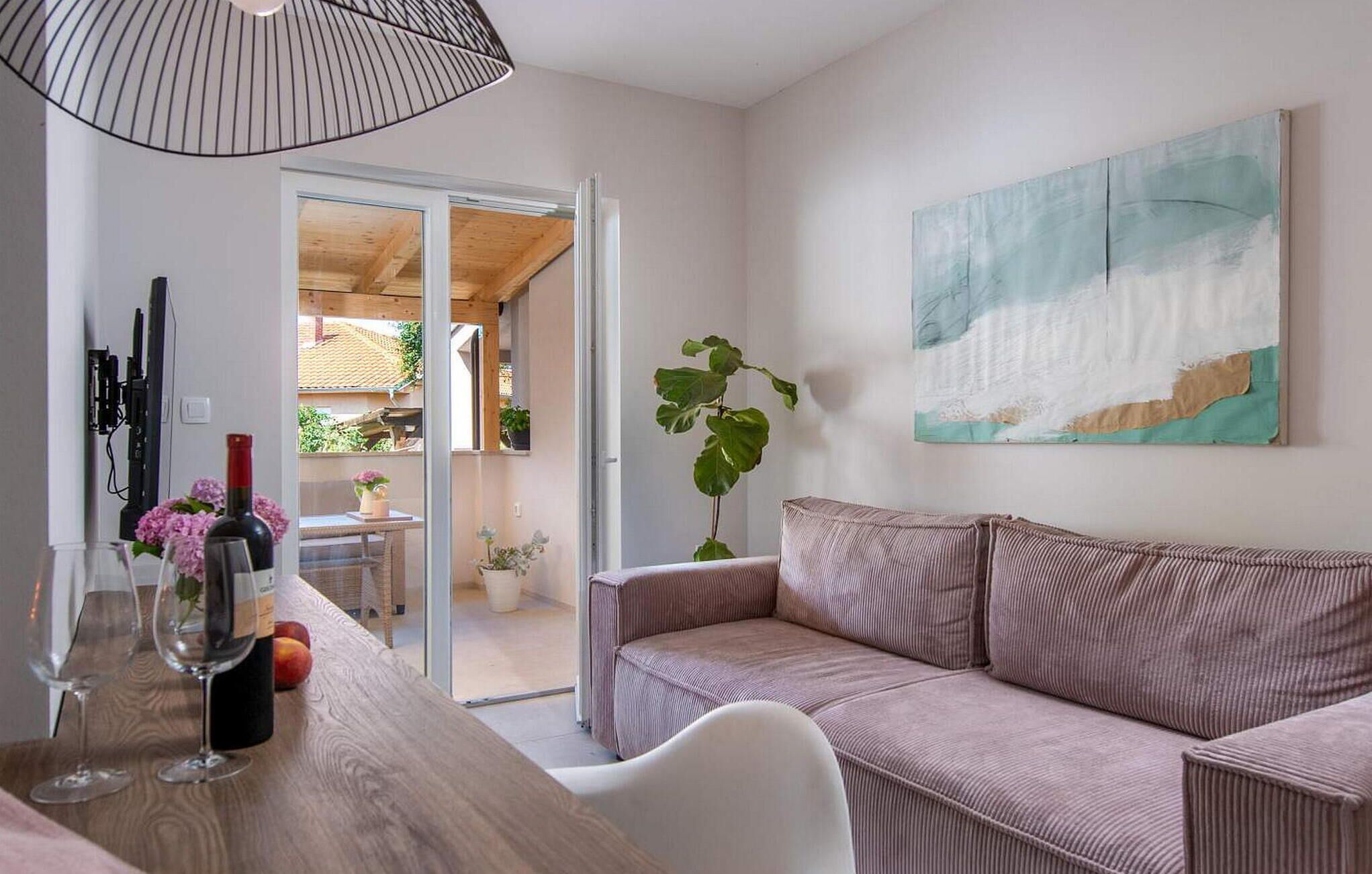 A modern living room with a sofa, a dining table with wine glasses, a large abstract painting, and a view of the outdoors.