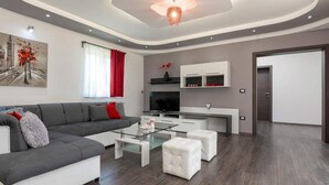 A modern living room with a grey sofa, white ottomans, a glass coffee table, and a flat-screen TV. - Lovely home in Motovun with WiFi (Motovun)