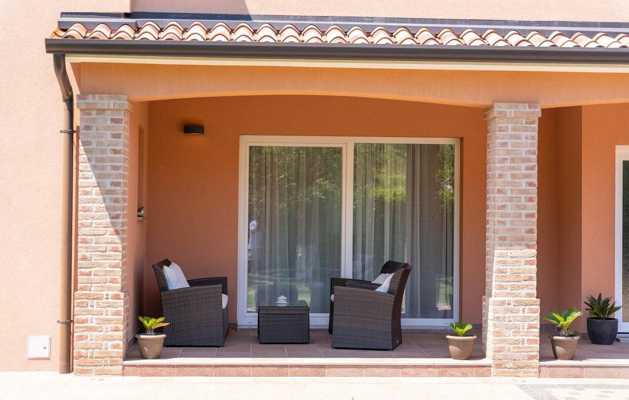 A covered outdoor seating area with two wicker chairs and a small table, flanked by potted plants.