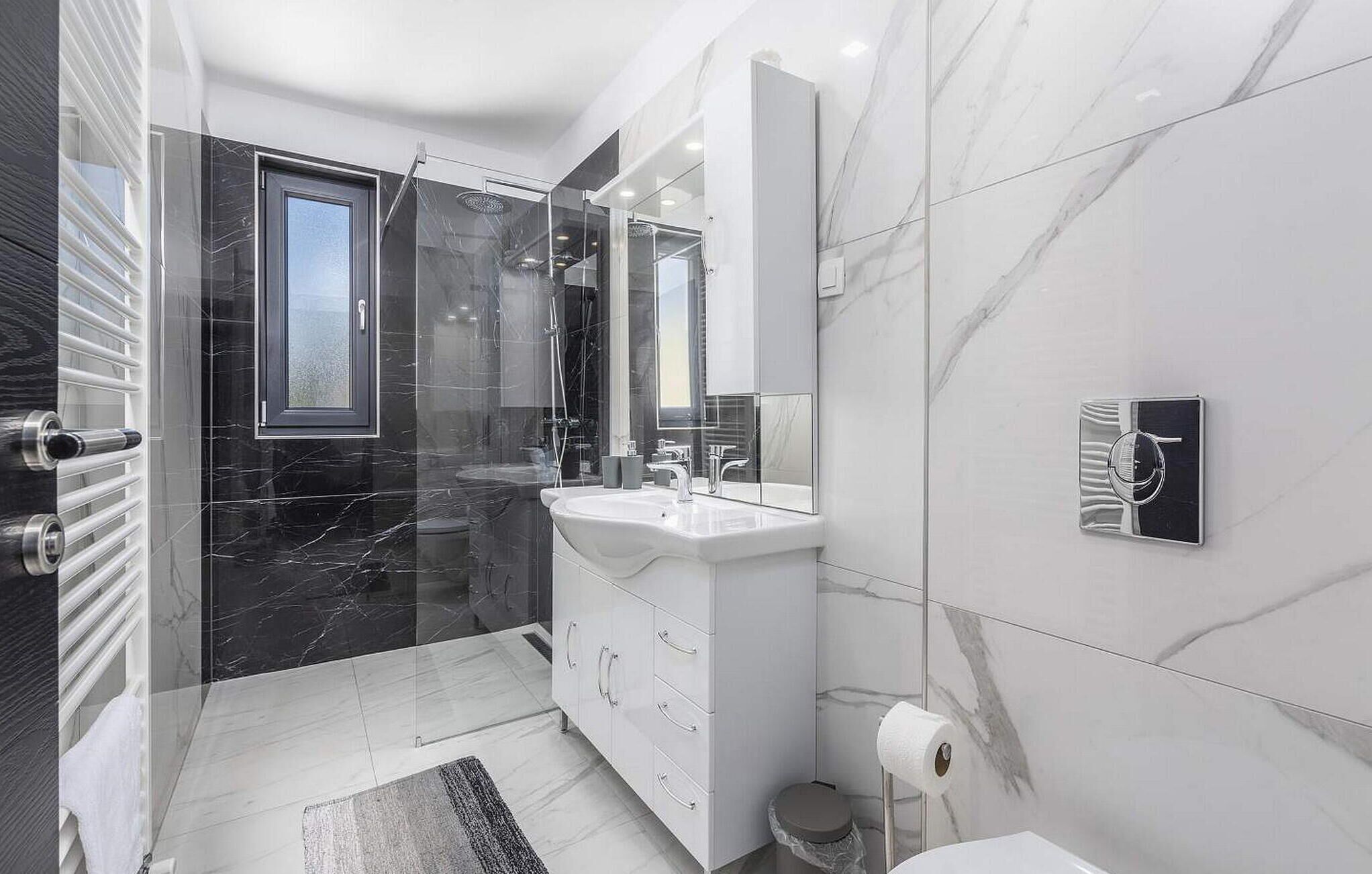 A modern bathroom with a glass-enclosed shower, a white vanity with a large mirror, and a marble backsplash.