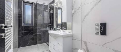 A modern bathroom with a glass-enclosed shower, a white vanity with a large mirror, and a marble backsplash.