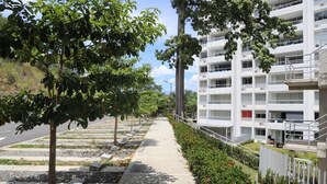 Un edificio residenziale moderno a più piani con facciata bianca e lineare, una scala centrale e un’area giardino curata con alberi e arbusti.