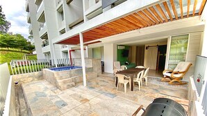 Un patio con pavimento in pietra, un barbecue, un tavolo da pranzo con sedie e un pergolato in legno.