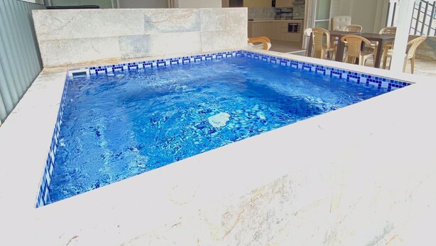 Una piscina rettangolare con piastrelle blu, un soffitto in legno e un bordo rivestito in pietra.
