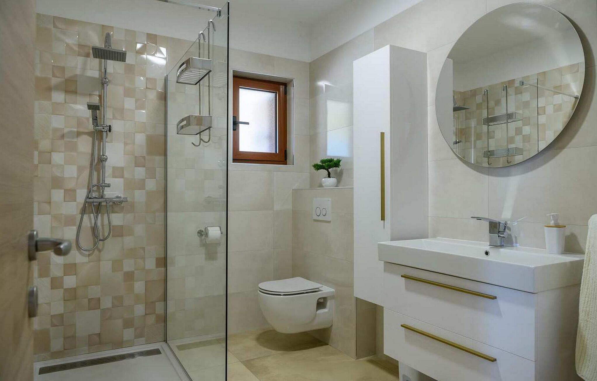 Ein modernes Badezimmer mit einer Duschkabine, einer Toilette, einem Waschbecken mit goldenen Armaturen und einem runden Spiegel.