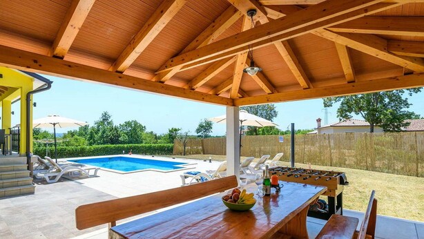 Un espacio al aire libre cubierto con piscina, sillas de descanso, una mesa de fútbol de mesa y un banco de madera.