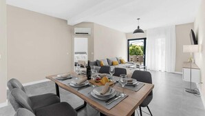 A modern dining area with a wooden table set for four, a sofa with cushions, and a view of a garden through a glass door. - Awesome home in Porec (Porec)