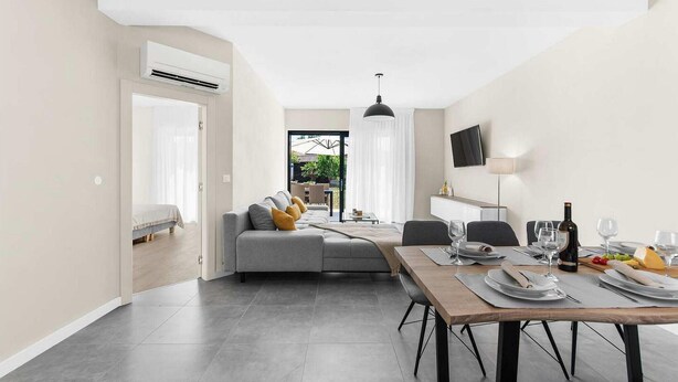 A modern dining area with a wooden table set for two, a sofa with cushions, and a TV mounted on the wall. - Awesome home in Porec (Porec)