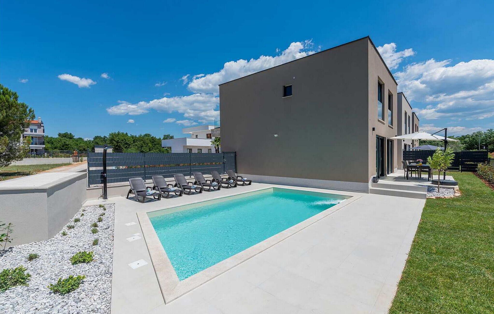 Ein moderner Poolbereich mit einem rechteckigen Pool, Liegestühlen und einem Gebäude mit flachem Dach.