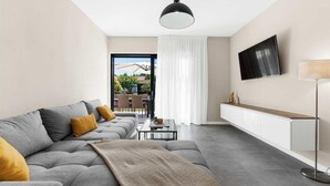 A modern living room with a grey sofa, a coffee table, a TV mounted on the wall, and a view of the outdoors through a glass door. - Awesome home in Porec (Porec)