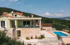 Una casa moderna de dos pisos con piscina, mobiliario exterior y vistas de las colinas circundantes.