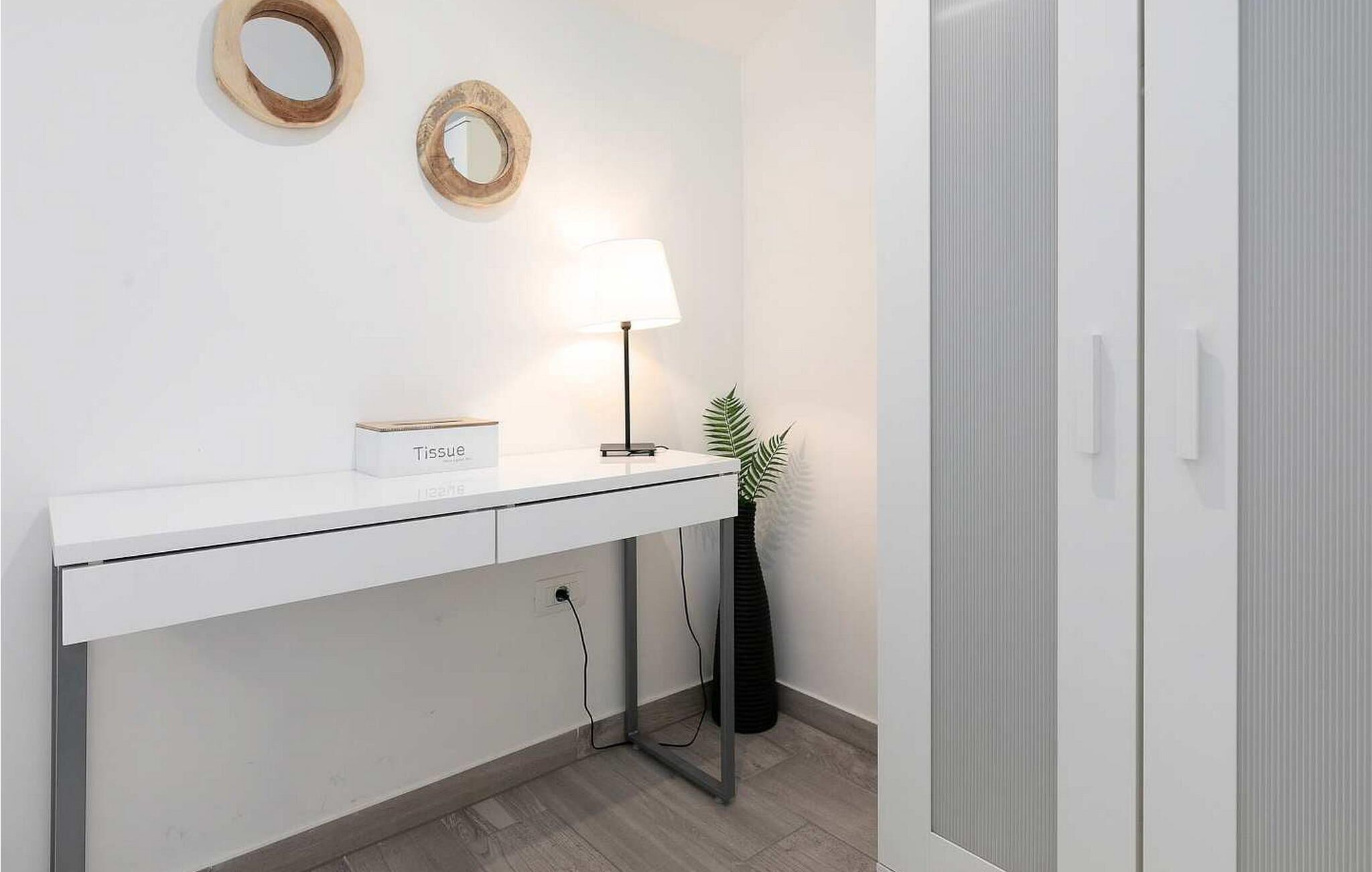 Een moderne badkamer met een witte wastafel, een doos zakdoekjes, een lamp en een pot met een plant.