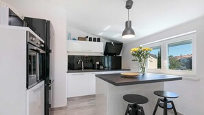 Uma cozinha moderna com uma ilha central, dois banquetes, uma luminária pendente e vista para o exterior através de uma janela.