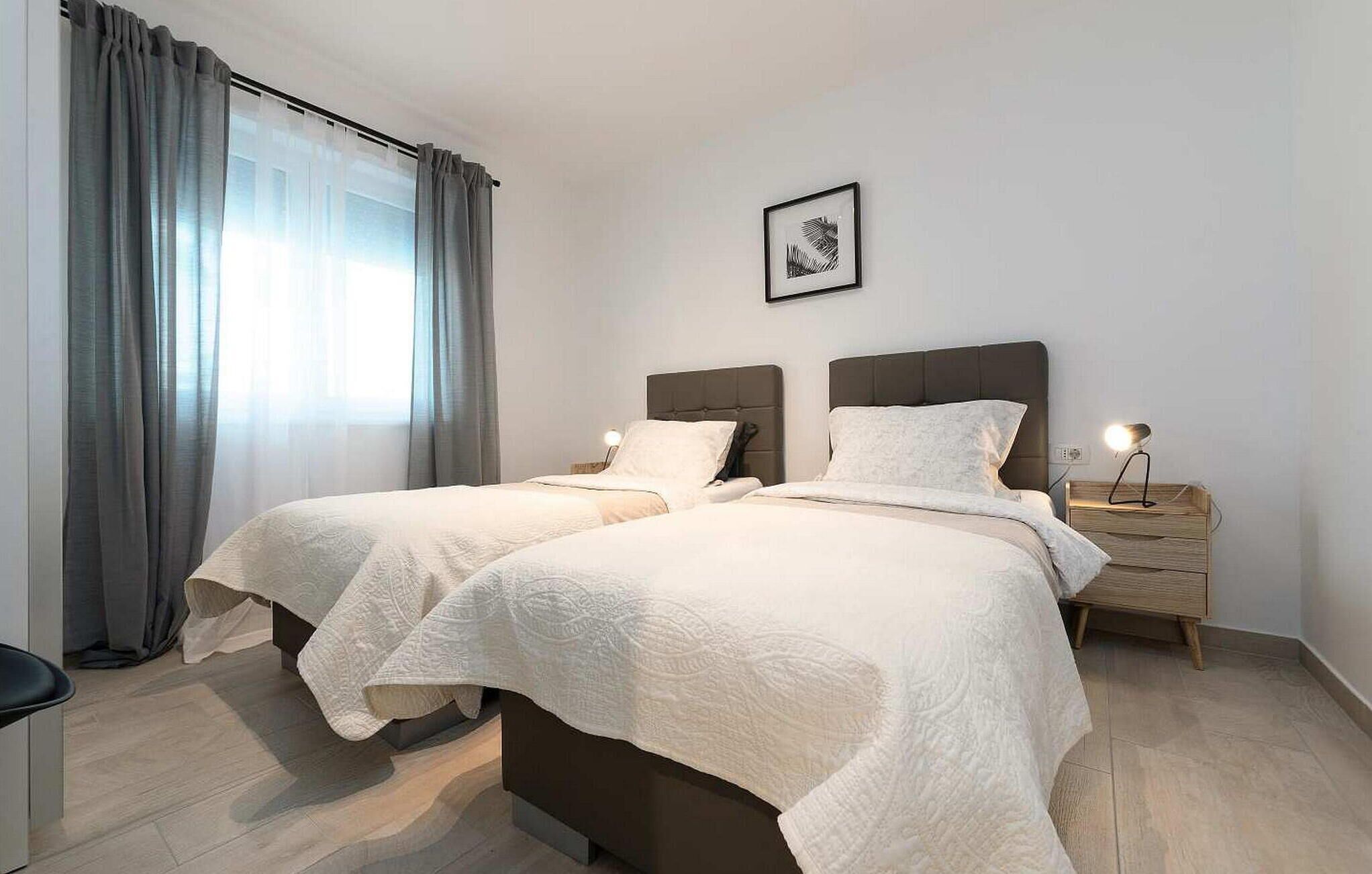 Une chambre double avec deux lits, une table de chevet avec une lampe, un tableau encadré au mur et une fenêtre avec des rideaux.