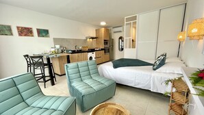 Un espacio habitable compacto con kitchenette, comedor, cama y zona de estar con una mesa redonda de madera.
