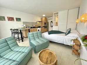 A compact living space with a kitchenette, a dining area, a bed, and a seating area with a round wooden table.