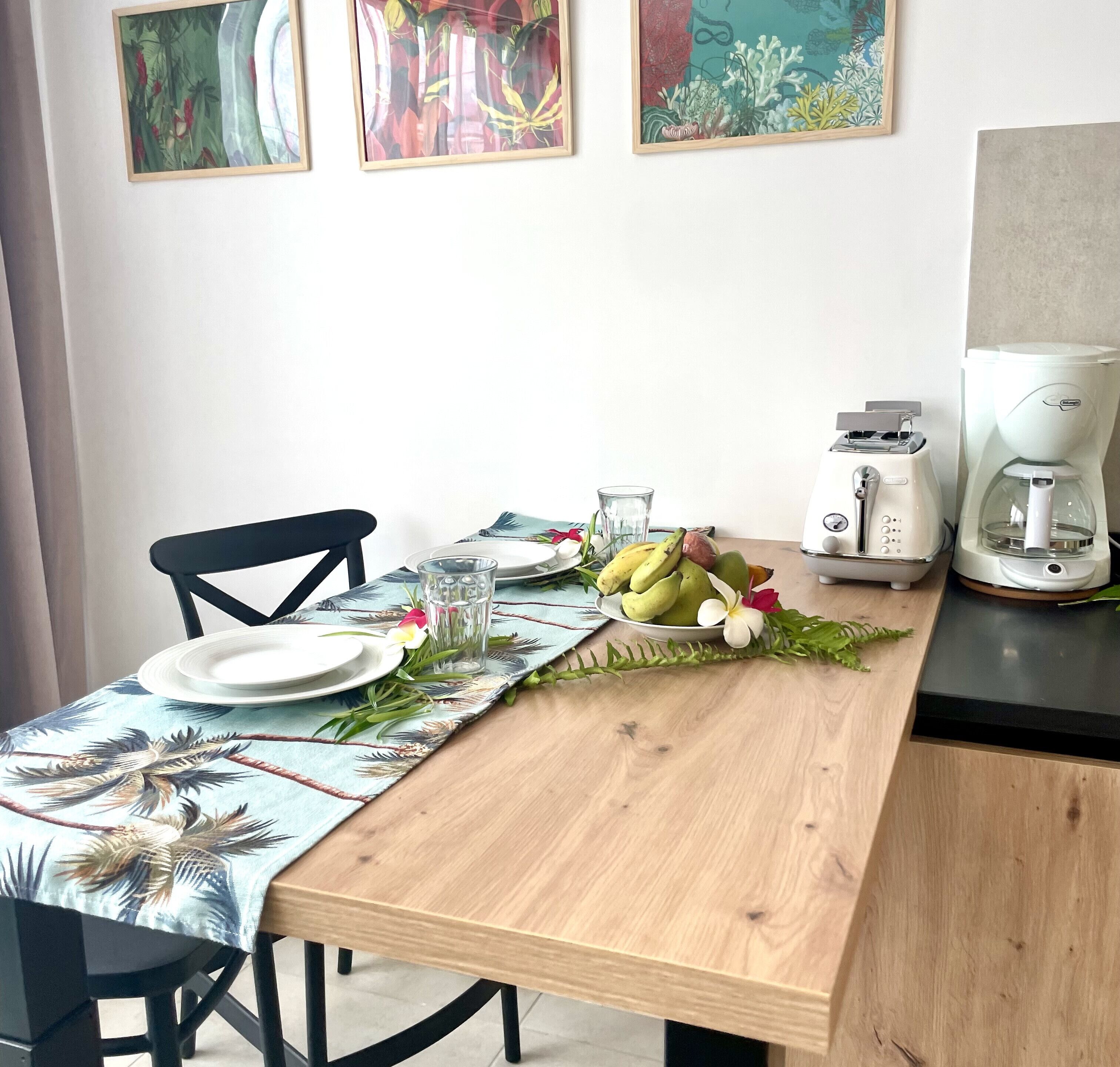 Un comedor con una mesa de madera, sillas, una cafetera y un frutero.