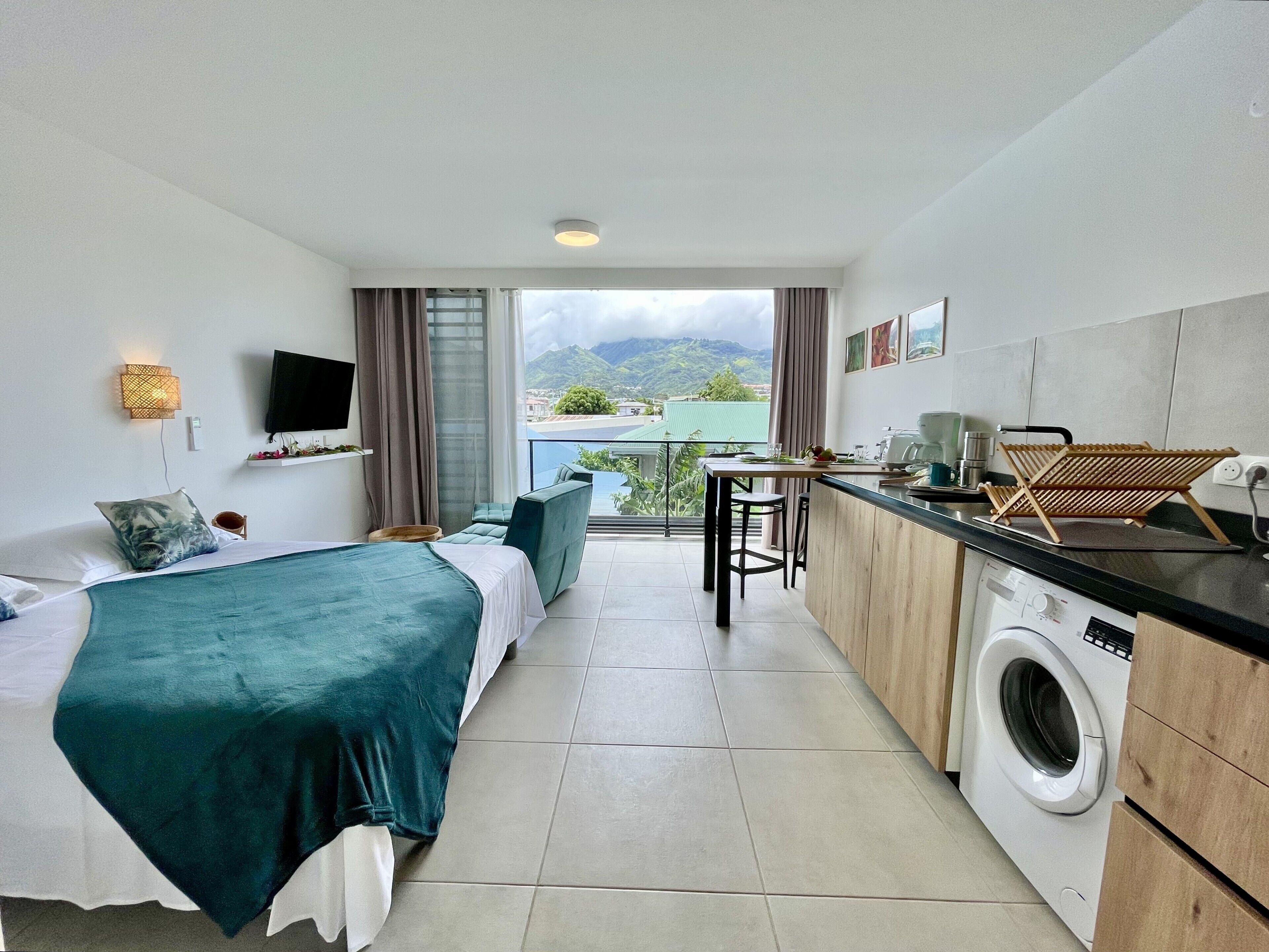 Une chambre d’hôtel comprenant un lit, une petite kitchenette, un lave-linge et un balcon avec vue sur les montagnes.
