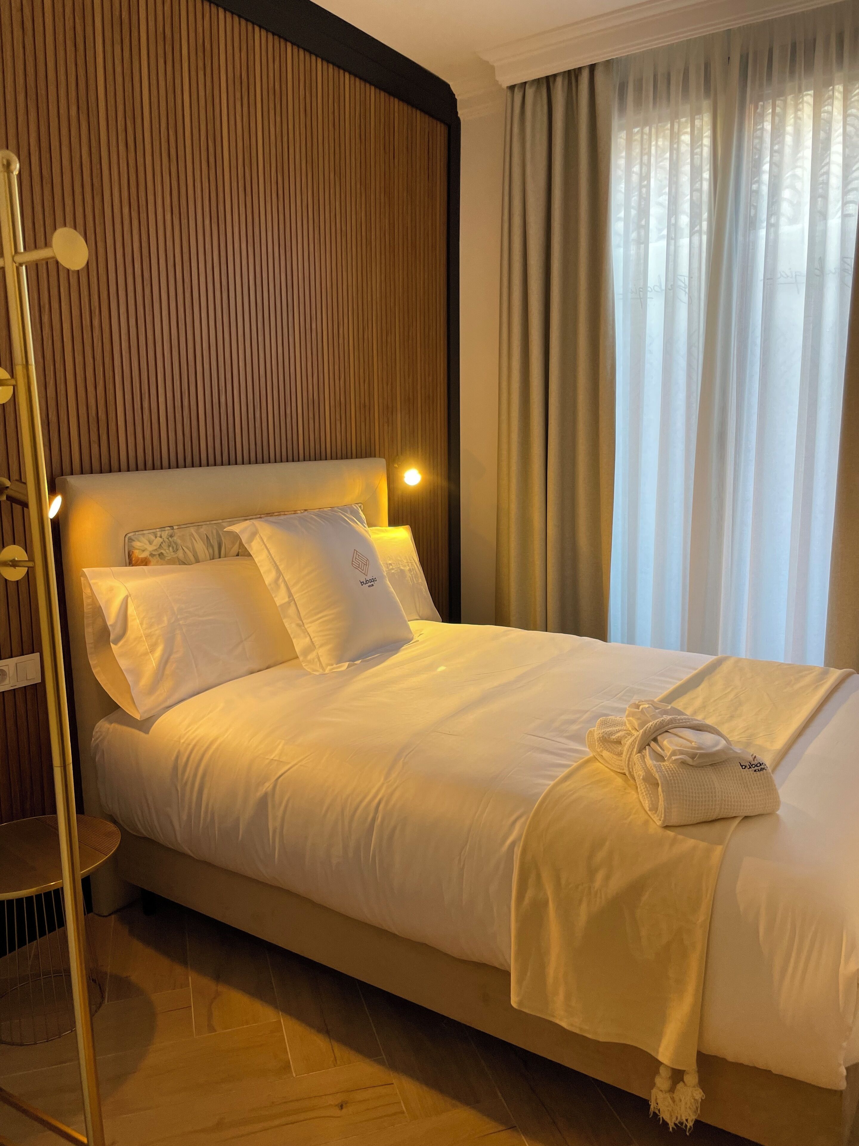 A neatly made bed with white linens and pillows, a bedside lamp, and a towel on the bed.