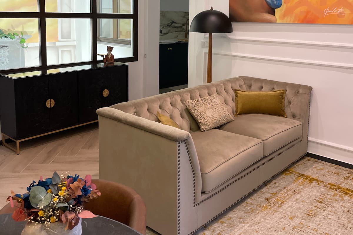 A living room with a beige sofa, a black cabinet, a large painting, and a vase with flowers.