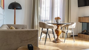 Ein modernes Wohnzimmer mit einer Couch, zwei Sesseln, einem runden Tisch, einer Stehlampe und einem an der Wand montierten Fernseher.