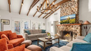 A living room with a stone fireplace, a chandelier, and a sofa set. - Historic Lux Retreat | Pool, Spa + 6 En-Suite Beds (Tucson)