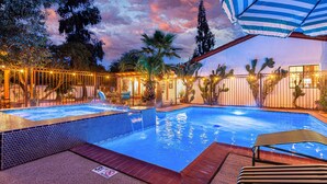 A swimming pool with a tiled edge, surrounded by a fence, palm trees, and a sunset sky. - Historic Lux Retreat | Pool, Spa + 6 En-Suite Beds (Tucson)