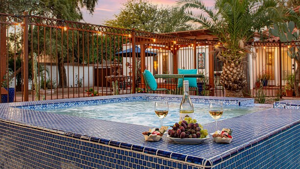 A pool area with a tiled edge, a bottle of wine, and a bowl of grapes. - Historic Lux Retreat | Pool, Spa + 6 En-Suite Beds (Tucson)