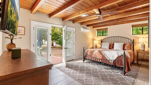 A bedroom with a bed, a wooden ceiling, a door leading outside, and a small table with a vase. - Historic Lux Retreat | Pool, Spa + 6 En-Suite Beds (Tucson)