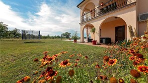 A large house with a spacious lawn, a tennis court, and a balcony with potted plants.