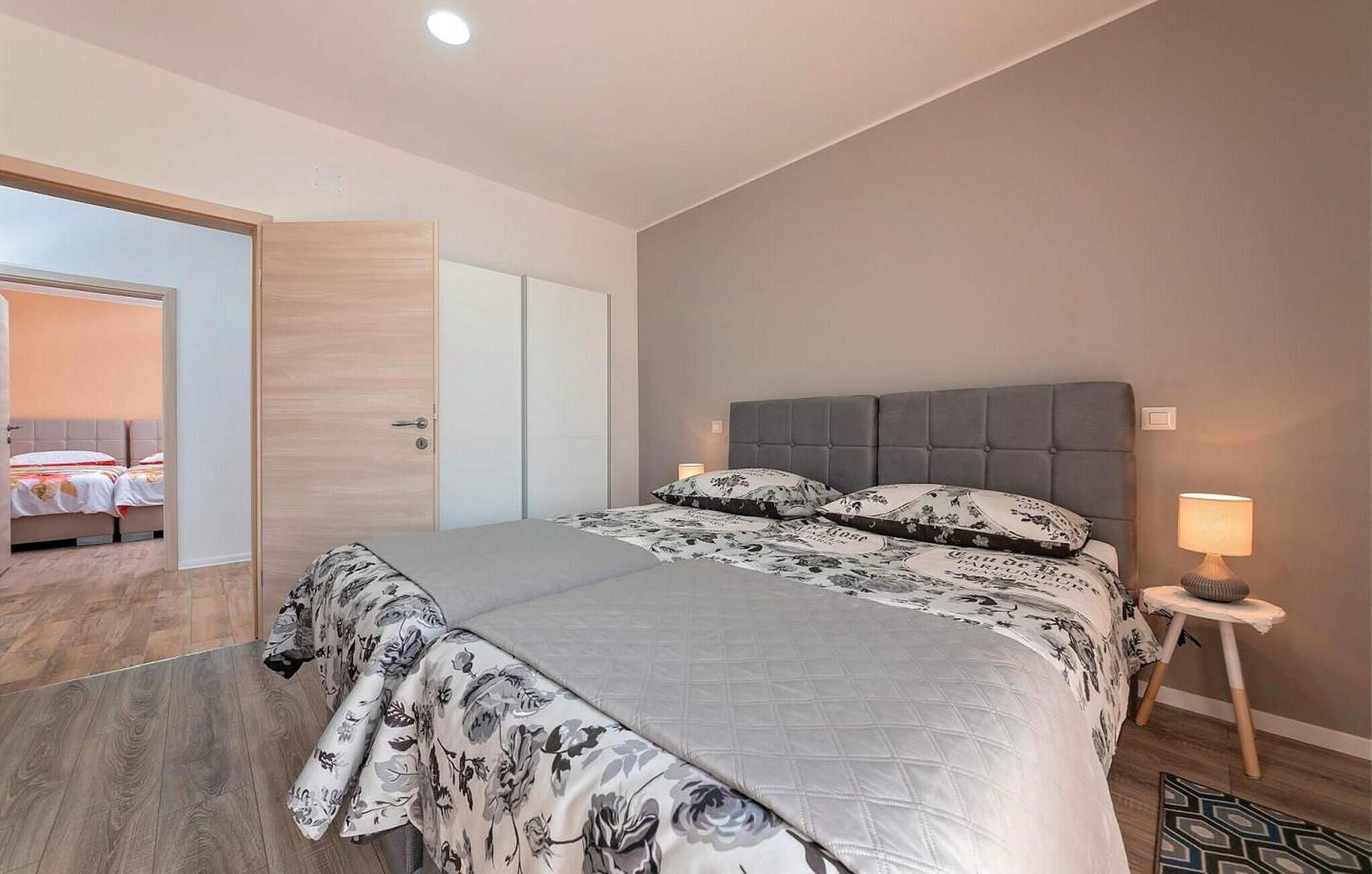 Un dormitori amb un llit, una tauleta de nit, una làmpada i una porta que dona a una altra habitació.
