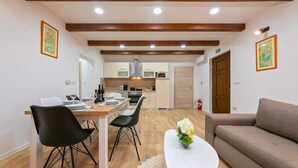 A modern kitchen with wooden beams, a dining area with black chairs, a white table, and a brown sofa.