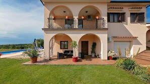 A two-story house with a balcony, a pool, and a well-maintained lawn.