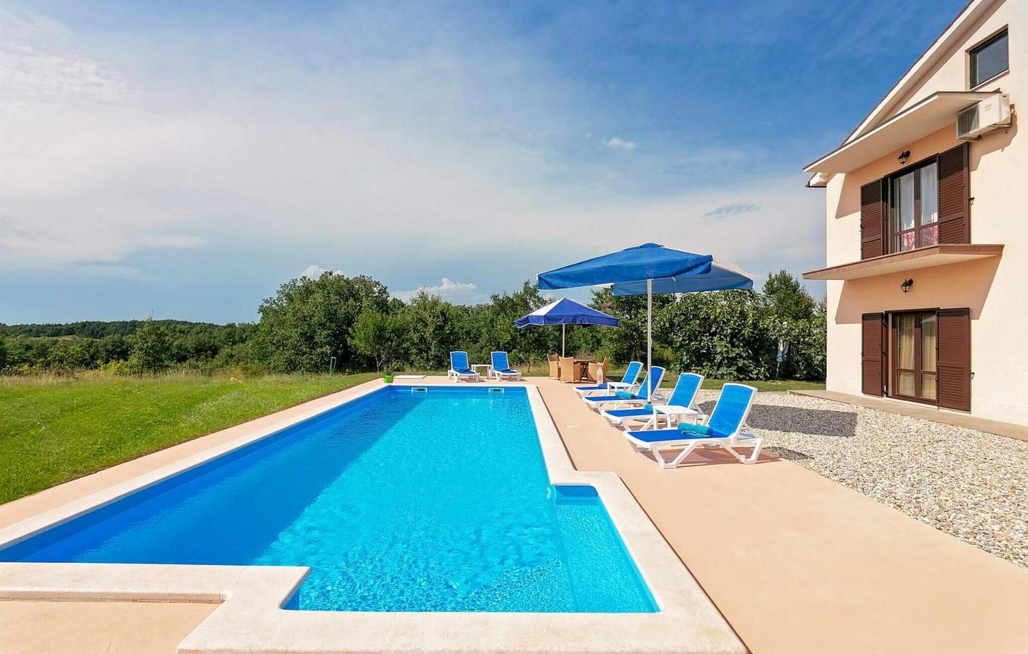 Una piscina amb aigua blava, envoltada de gandules i ombrelles, i un edifici amb un balcó.