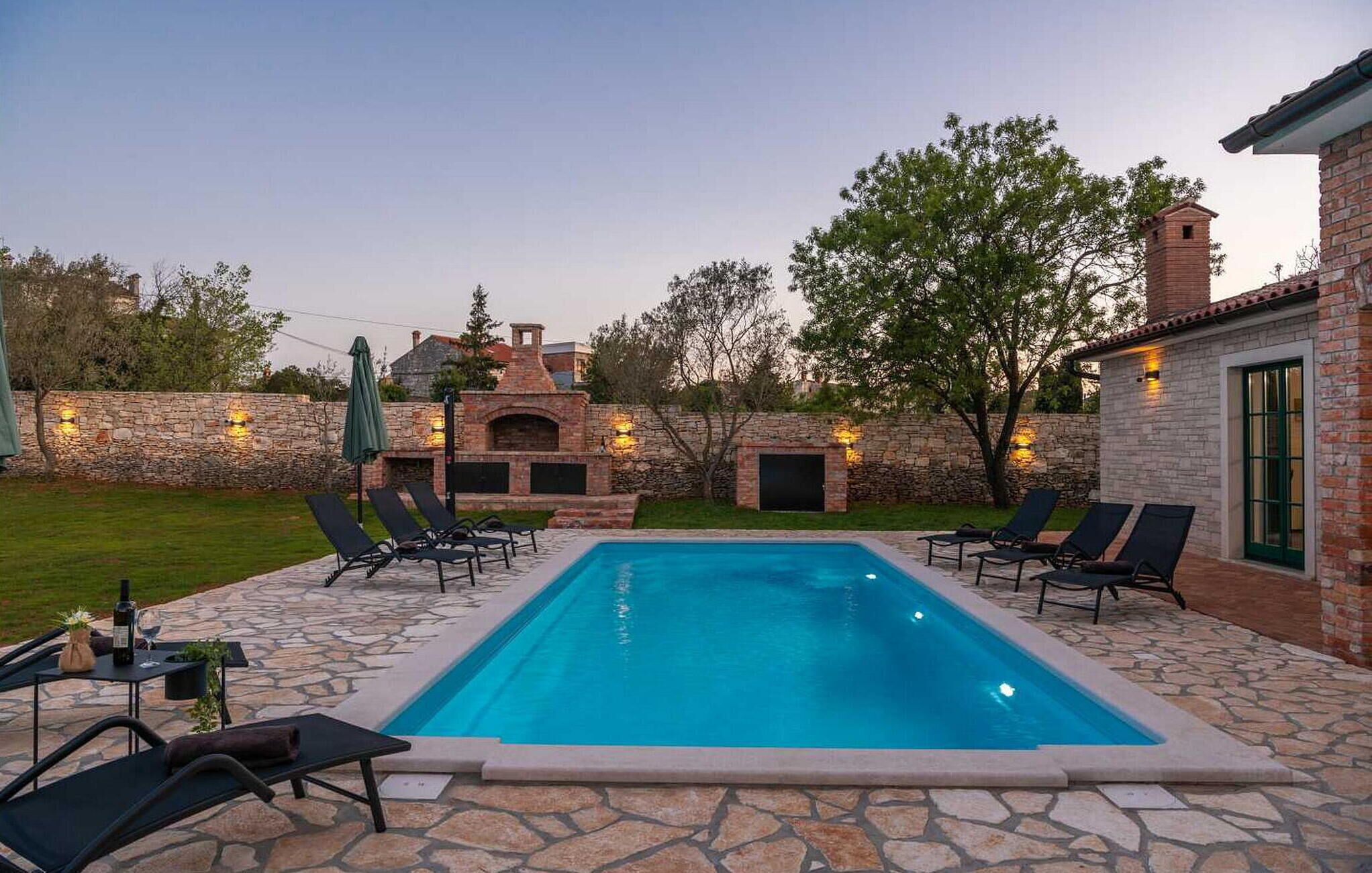 Una piscina rettangolare con sdraio e un patio in pietra.