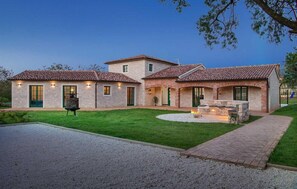 Une maison à deux étages avec une façade en pierre, un patio doté d’un foyer et une pelouse bien entretenue.