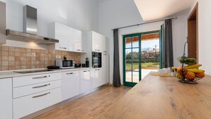 A modern kitchen with white cabinets, a microwave, and an oven. There's a wooden table with fruit and a view of the outdoors through a glass door. - Beautiful home in Vodnjan (Vodnjan)